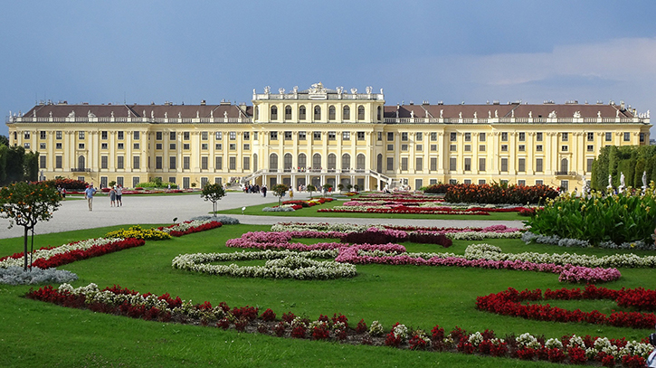 Schloss Schönbrunn mit gepflegter Gartenanlage und blühenden Beeten im Vordergrund.