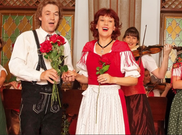 Sänger und Musiker in traditioneller Tracht bei einer Aufführung mit Blumen in der Hand.