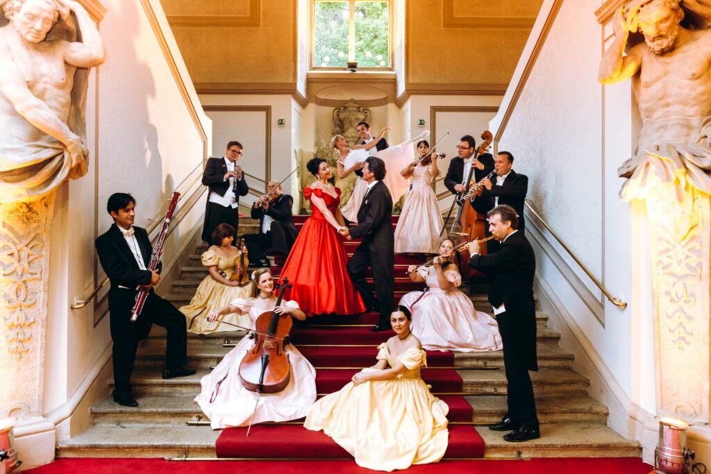 Musikerensemble auf einer breiten Treppe in einem prachtvollen Gebäude, während sie musizieren und tanzen.