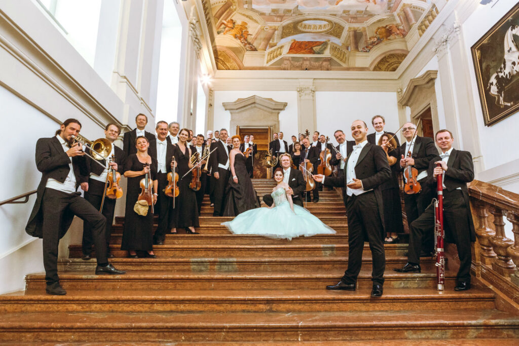 Musiker des Hofburg Orchesters in eleganter Kleidung auf einer Treppe vor ihrem Auftritt.