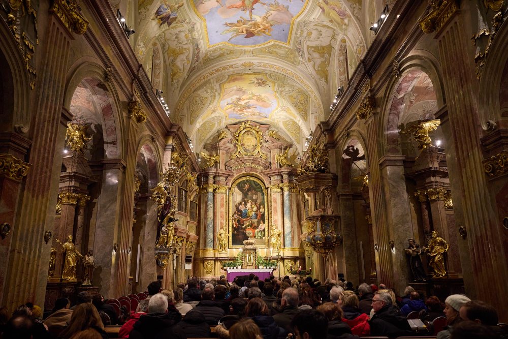 Publikum in einer barocken Kirche mit kunstvoll bemalten Decken und goldenen Verzierungen.