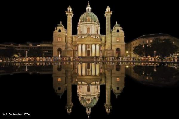 Die Karlskirche in Wien bei Nacht, wunderschön beleuchtet und im Wasser gespiegelt.